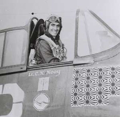 Pilot w hełmofonie uśmiecha się z kabiny myśliwca, na burcie pod kabiną rzędy japońskich flag