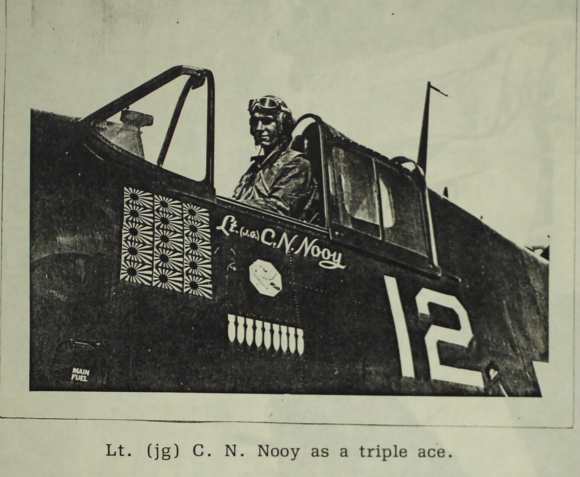 Pilot w pilotce siedzi w kabinie myśliwca, na burcie jego nazwisko, piętnaście japońskich flag i duża cyfra 12