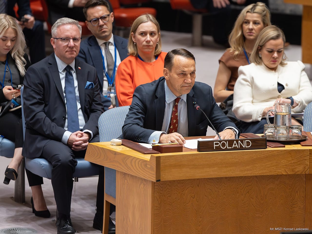 Radosław Sikorski przemawia przy stole z tabliczką Poland w sali Rady Bezpieczeństwa ONZ, za nim członkowie delegacji