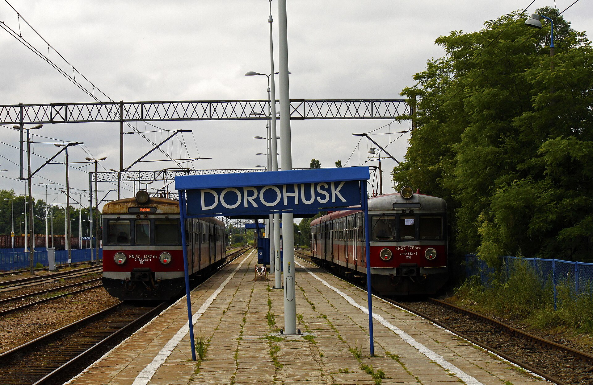 Peron z niebieską tablicą z napisem Dorohusk, po obu stronach dwa czerwono-kremowe pociągi elektryczne