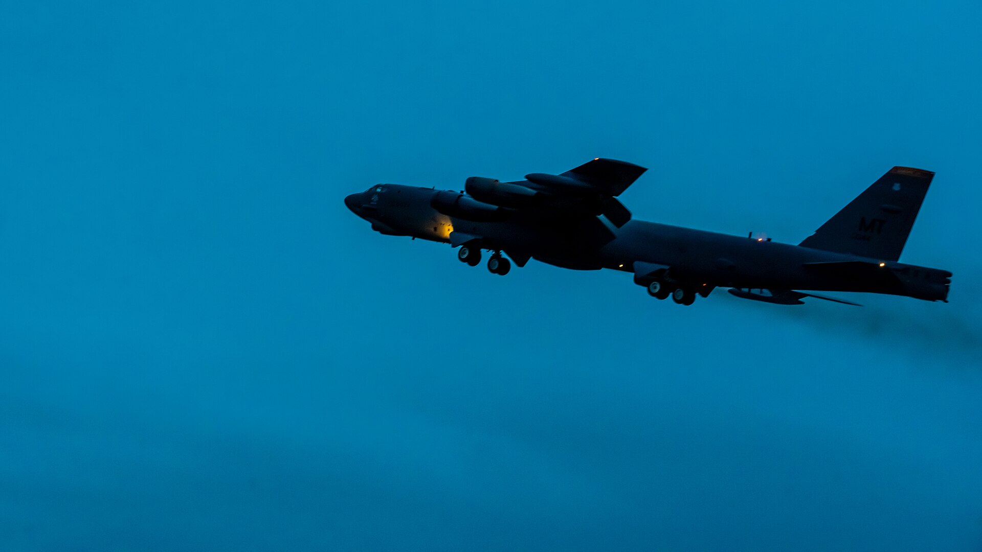 Ciemna sylwetka bombowca B-52 z wypuszczonym podwoziem na tle niebieskiego nieba o zmierzchu