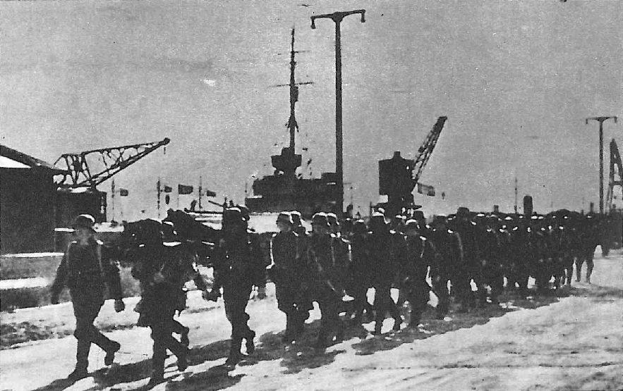 Kolumna niemieckich marynarzy maszeruje nabrzeżem Portu Wojennego Hel, w tle dźwigi i maszt okrętu, 2 października 1939