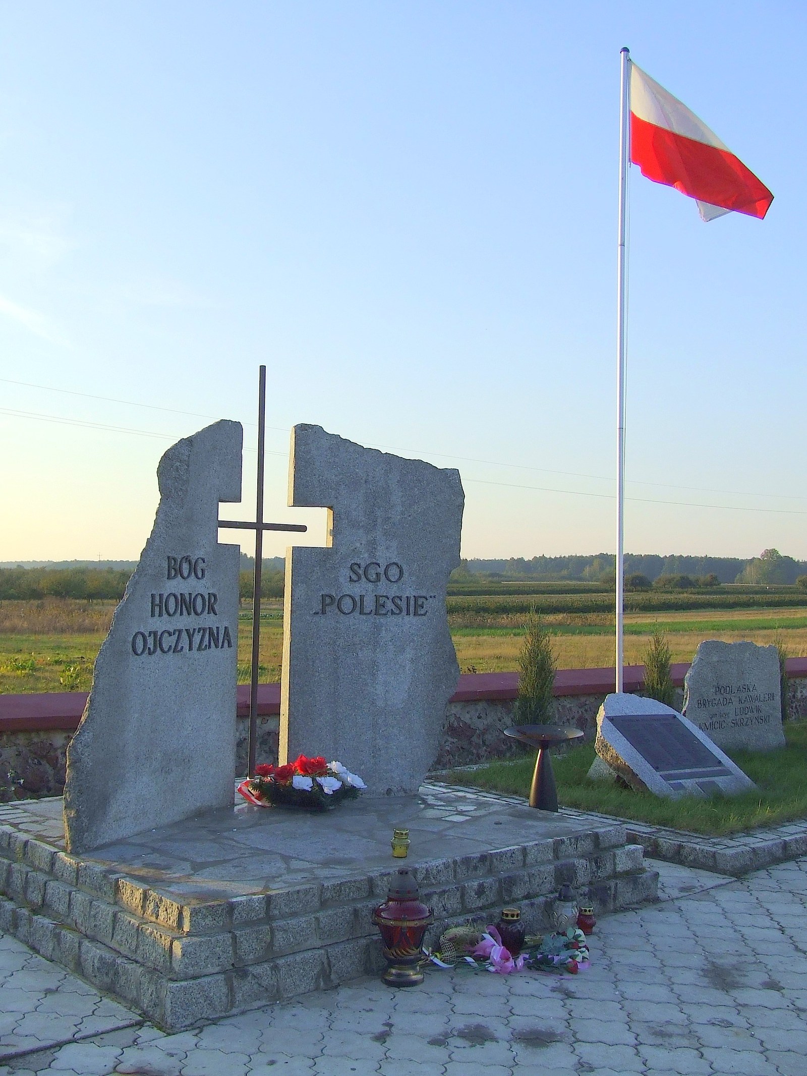 Pomnik z dwóch granitowych głazów z krzyżem i napisami Bóg Honor Ojczyzna oraz SGO Polesie, obok głaz Podlaskiej Brygady Kawalerii i biało-czerwona flaga