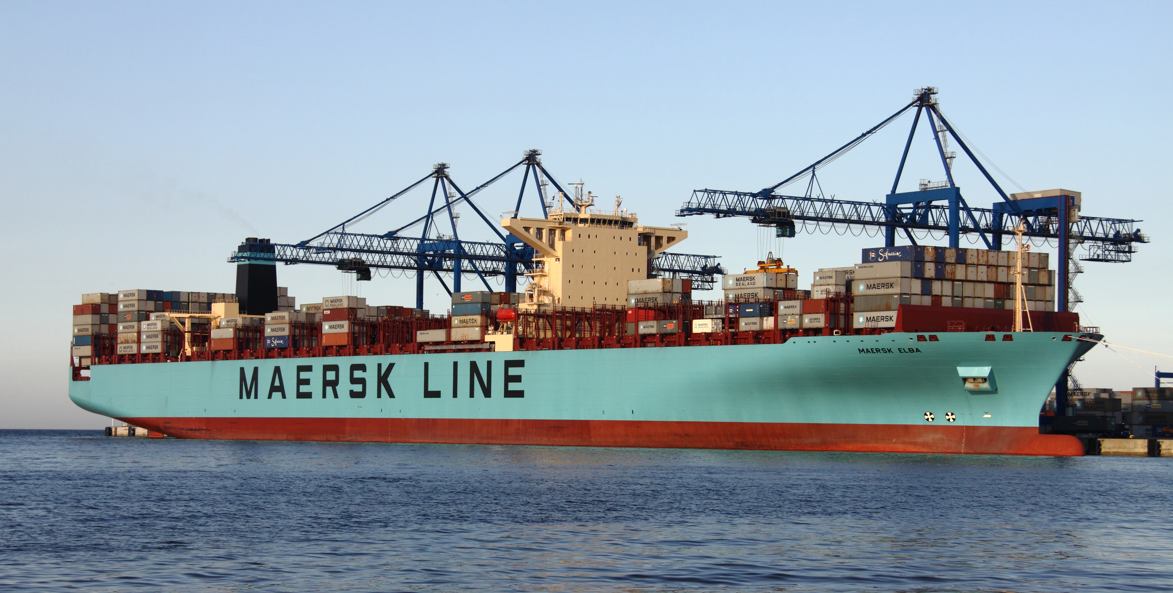 Wielki kontenerowiec morski Maersk z tysiącami kolorowych kontenerów płynący po spokojnej wodzie
