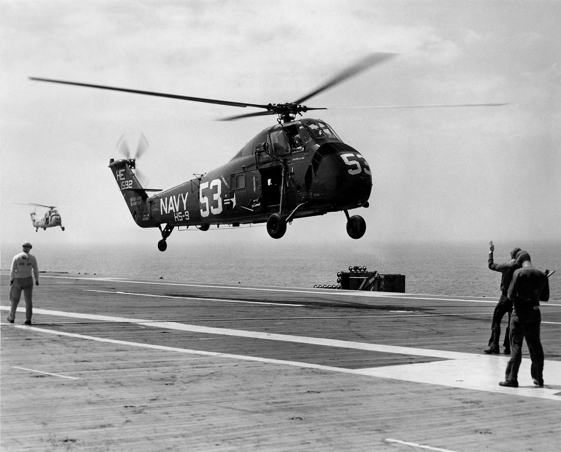 Śmigłowiec z numerem 53 i napisem Navy ląduje na pokładzie okrętu, obok stoją marynarze pokładowi